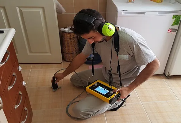 Electronic leak detection service technician inspecting pipes with specialized equipment.